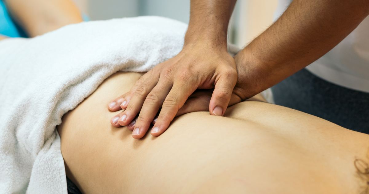Klassische Massagetherapie als Hausbesuch in München – Physiotherapie Köpple Therapeutin massiert den Rücken eines Patienten auf einer mobilen Massageliege